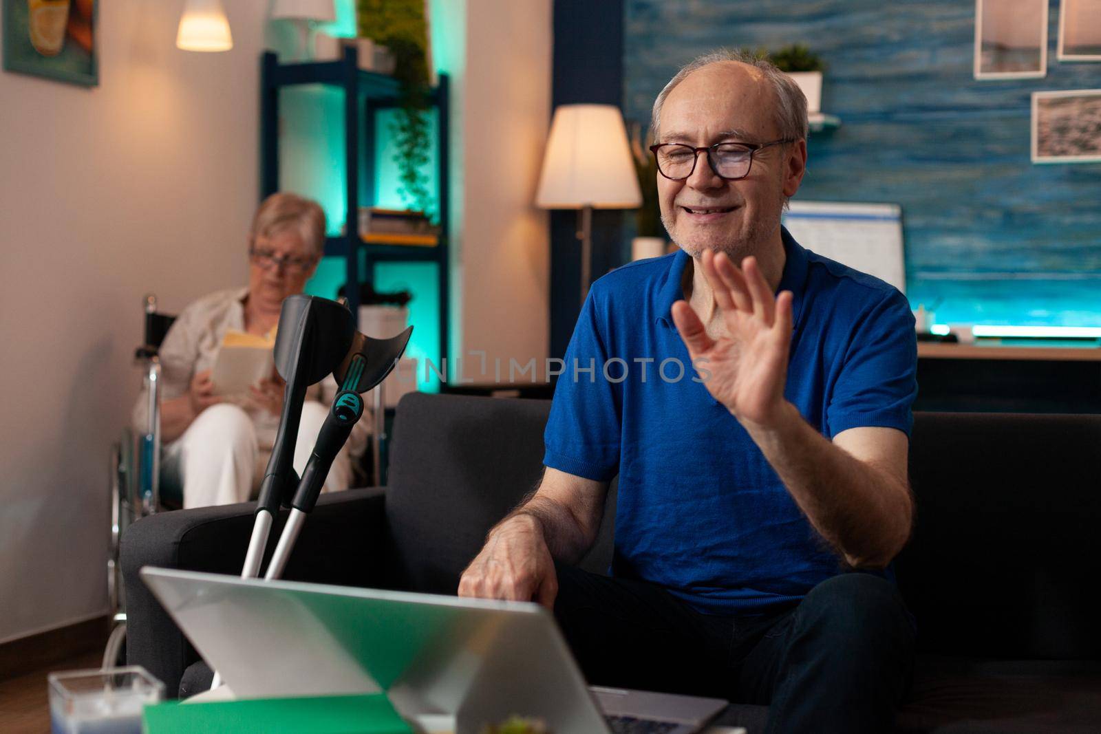 Elderly man waving at video call conference on laptop by DCStudio