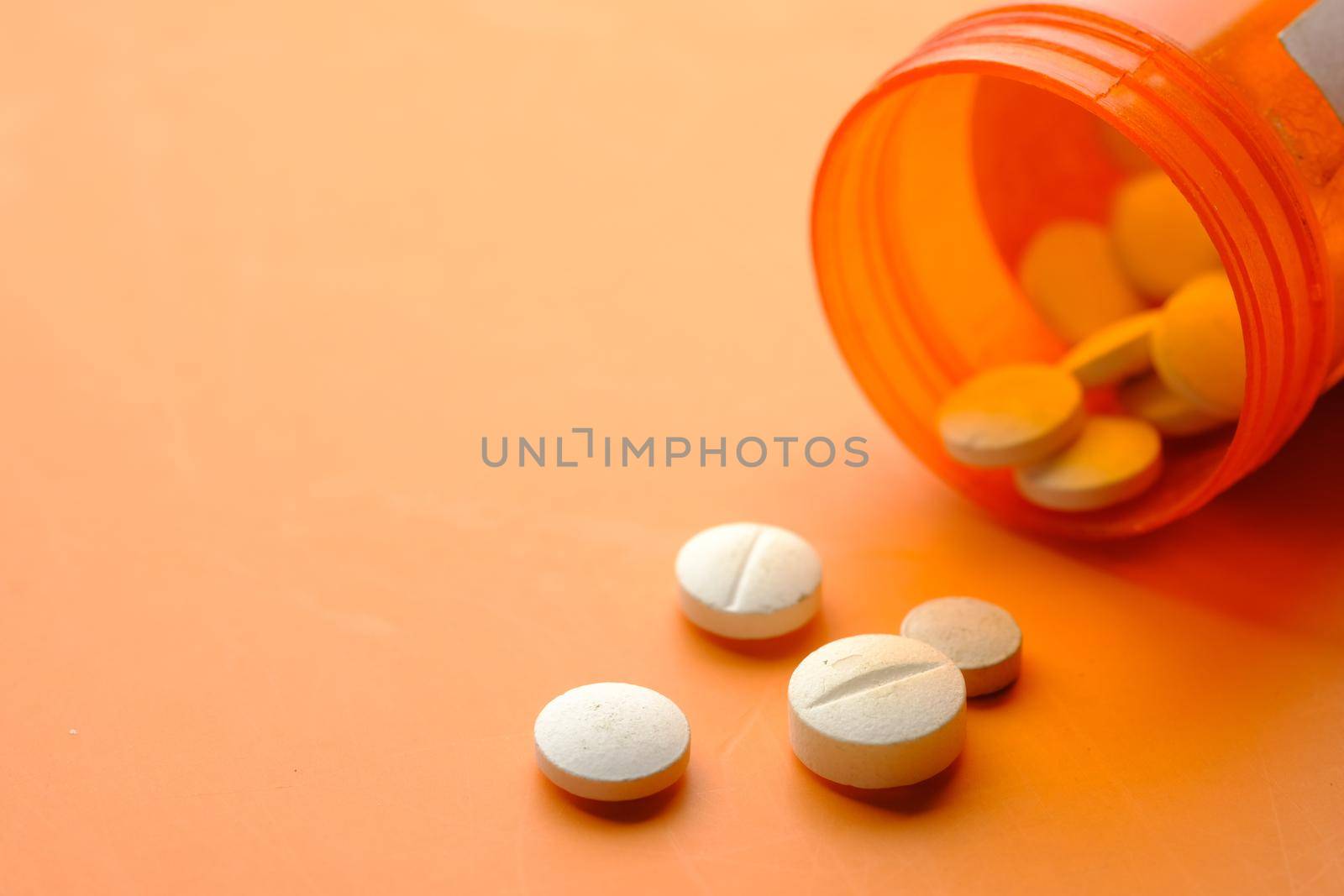 white color medical pills spilling on orange background .