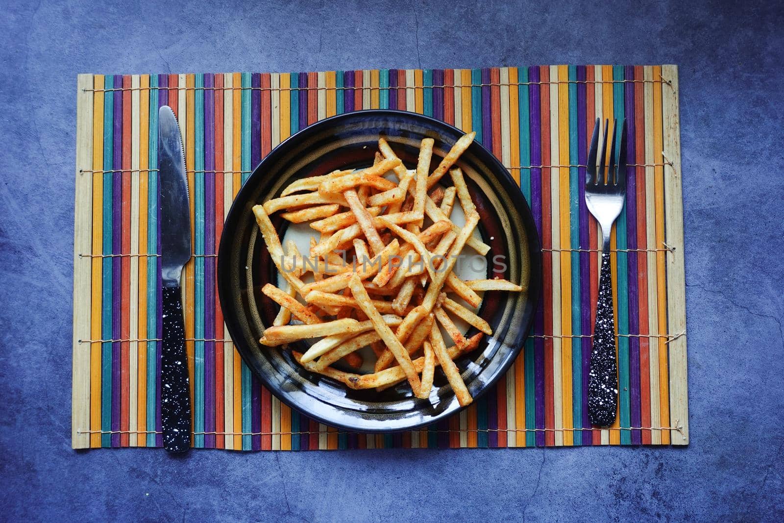 top view of french fries on a plate with cutlery on table .