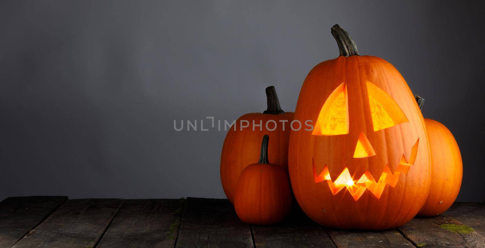 Glowing Halloween pumpkin head jack lantern on wooden table over gray background with copy space for text