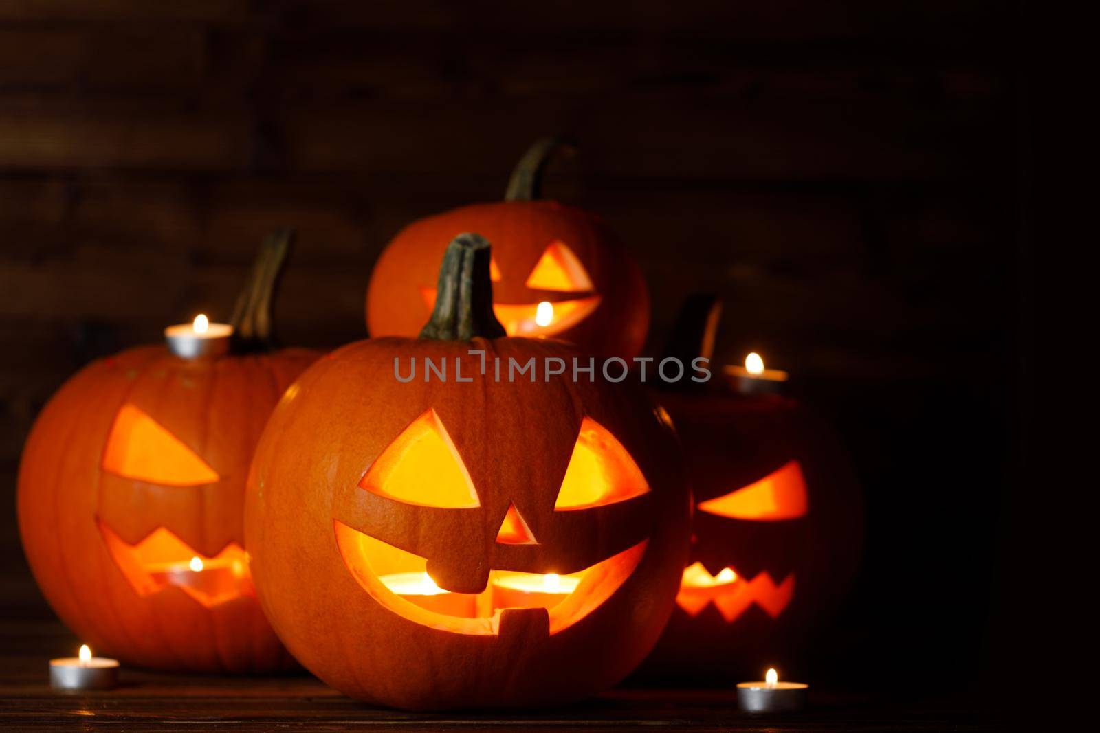 Group of glowing Halloween Pumpkin lanterns and burning candles on dark wooden background