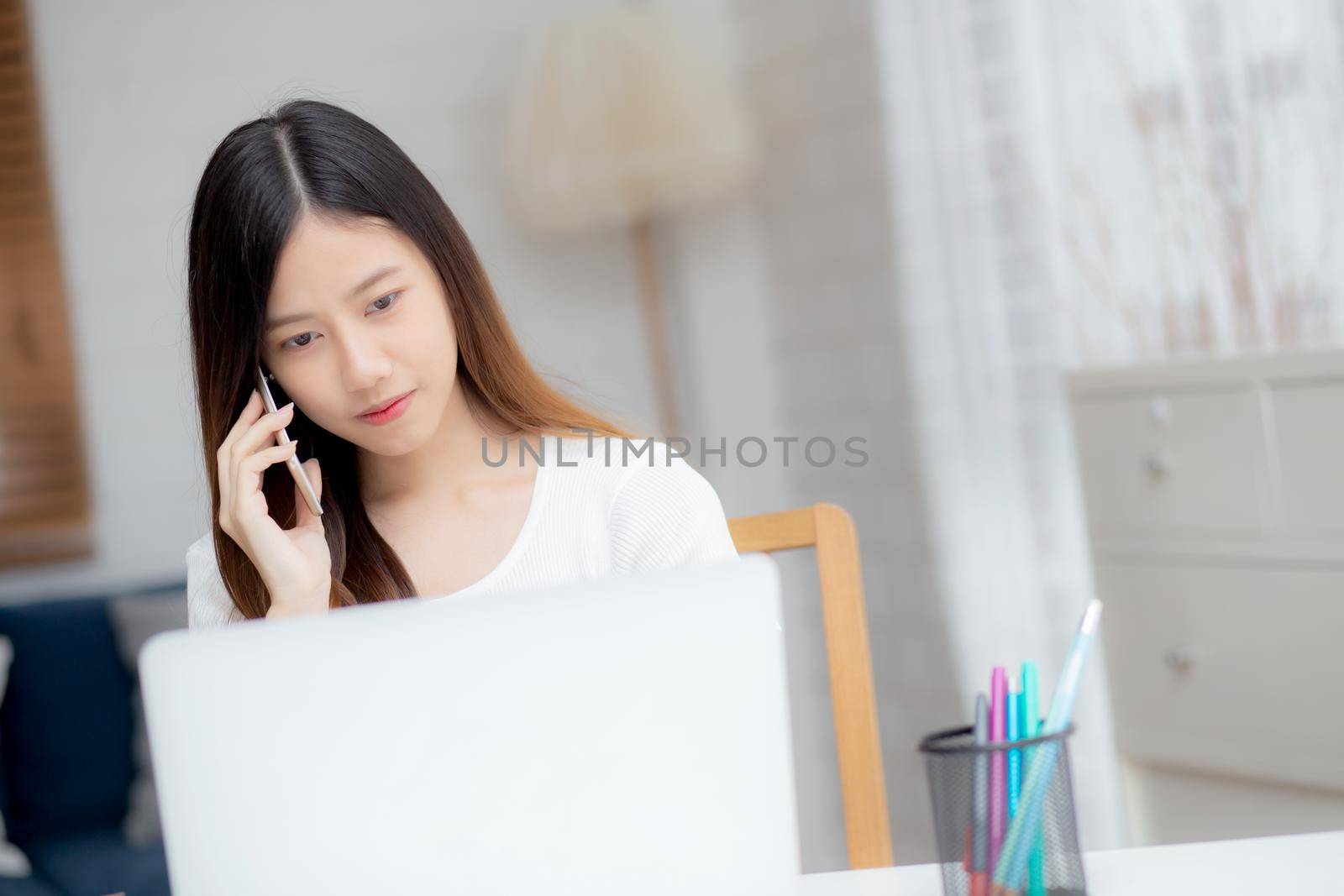 Young asian woman talking phone and work from home with laptop computer, freelance using notebook to internet online and speak on smartphone, domestic life, business and communication concept.