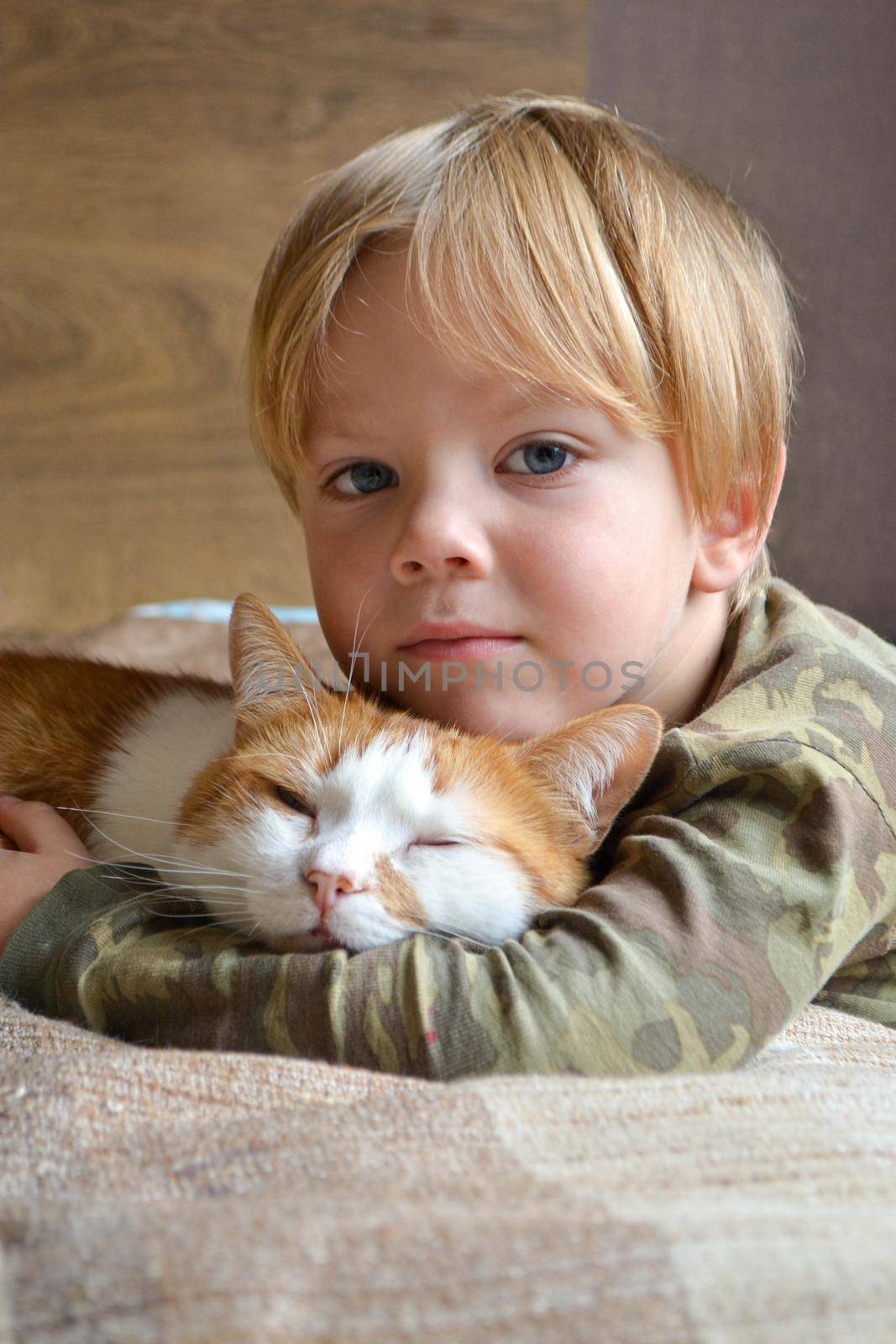 Portrait of happy adorablechild aged four years old on the bed in his room whit sleeping red cat. Thoughtful look. High quality photo