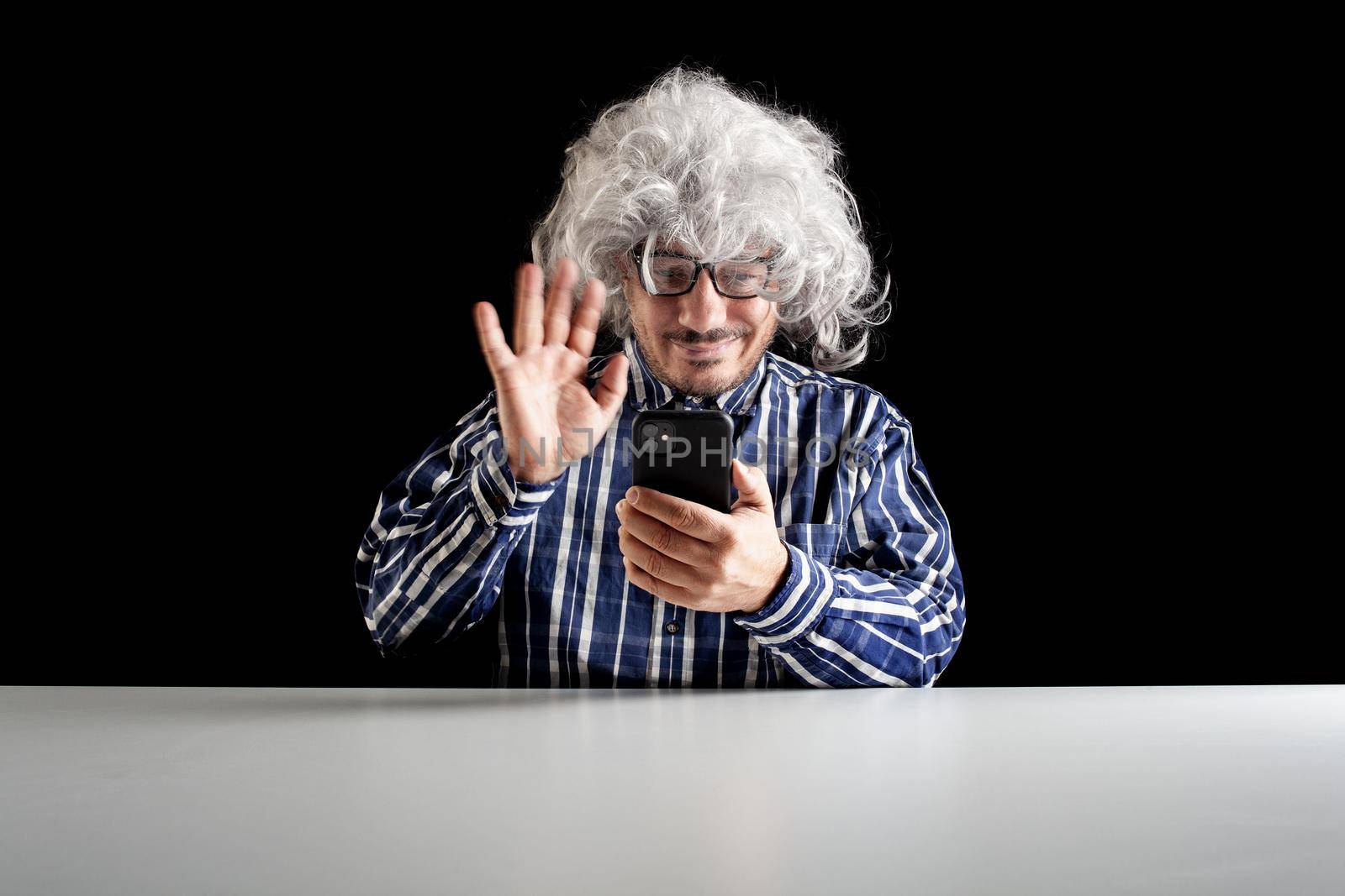 Smiling man sitting at the desk having a videochat talking on smartphone on black background