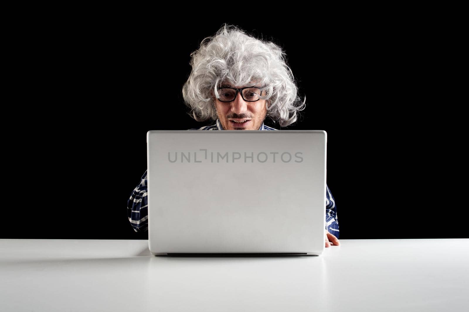 Smiling senior man with gray hair wearing a checkered shirt using laptop sit at the desk. Black background with copy space
