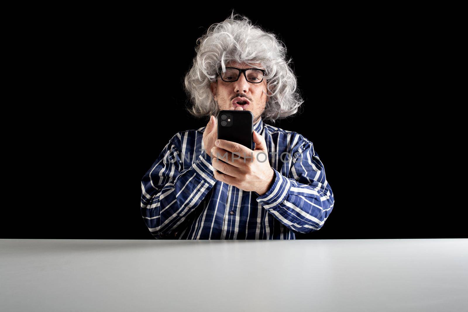 Man sitting at the desk blowing kiss having a videochat using a smartphone on black background