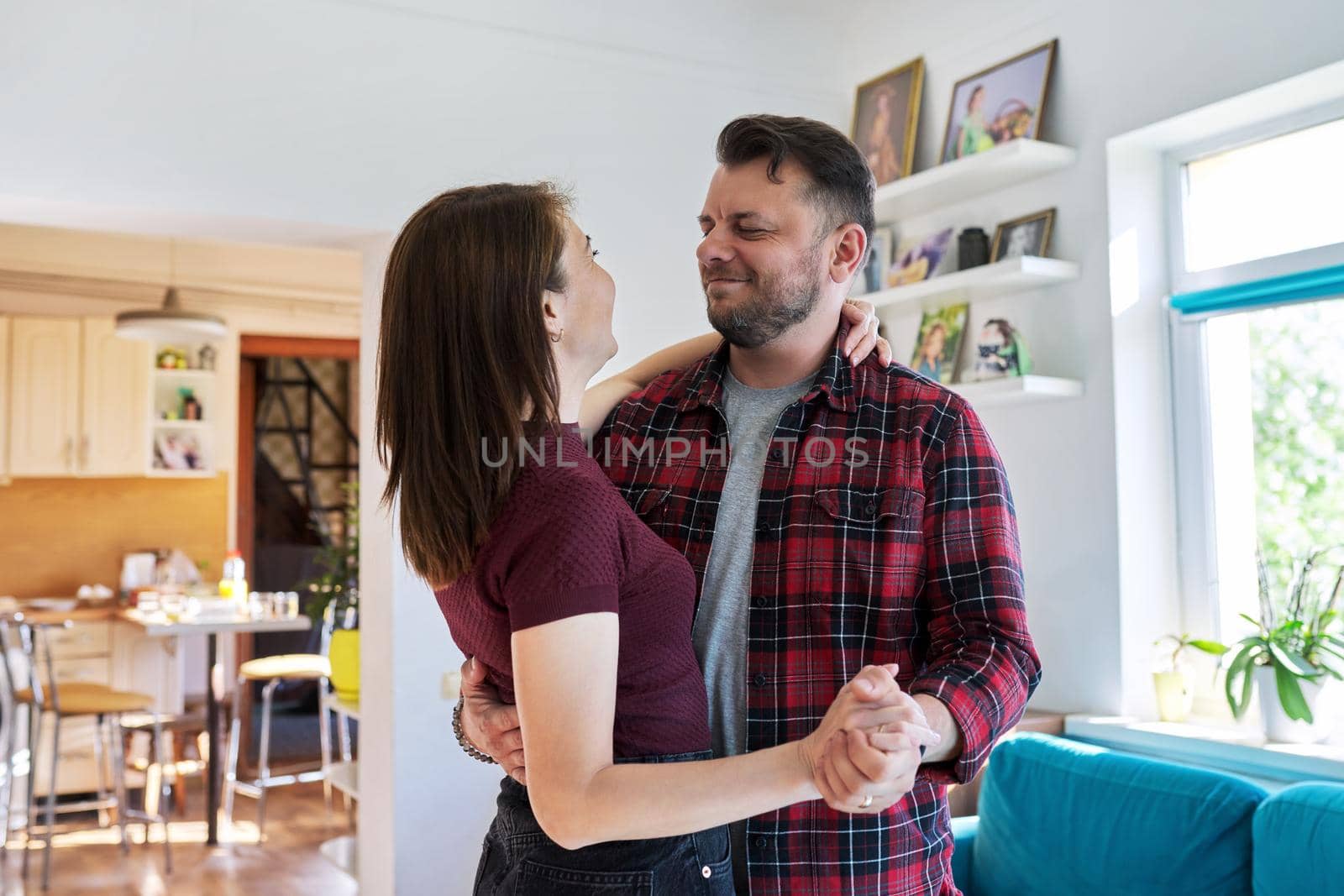 Happy romantic middle aged couple dancing at home. Loving husband and wife 40s of age are embracing and dancing in the living room. Family, relationship, date, mature age concept