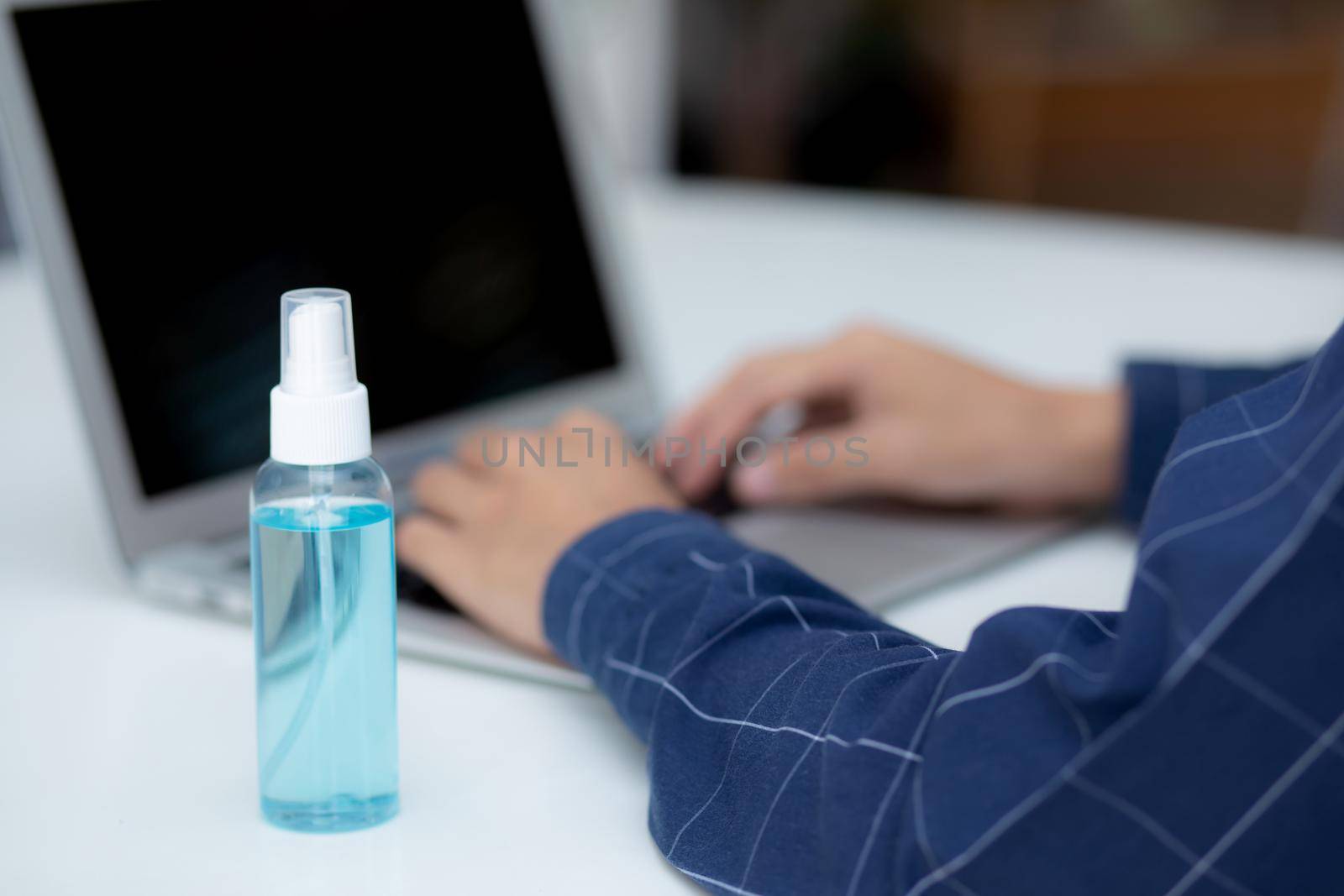 Hand of man work from home with alcohol gel or sanitizer for cleaning and protect coronavirus or covid-19, new normal, quarantine and social distancing, business and freelance using laptop computer. by nnudoo