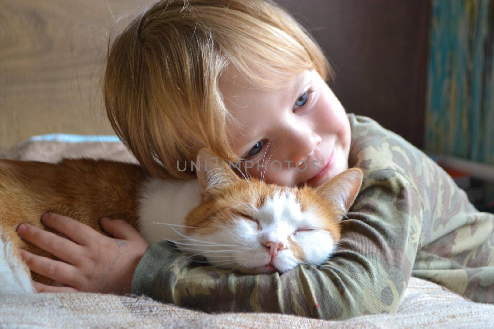 Portrait of happy adorablechild aged four years old on the bed in his room whit sleeping red cat. Thoughtful look. High quality photo