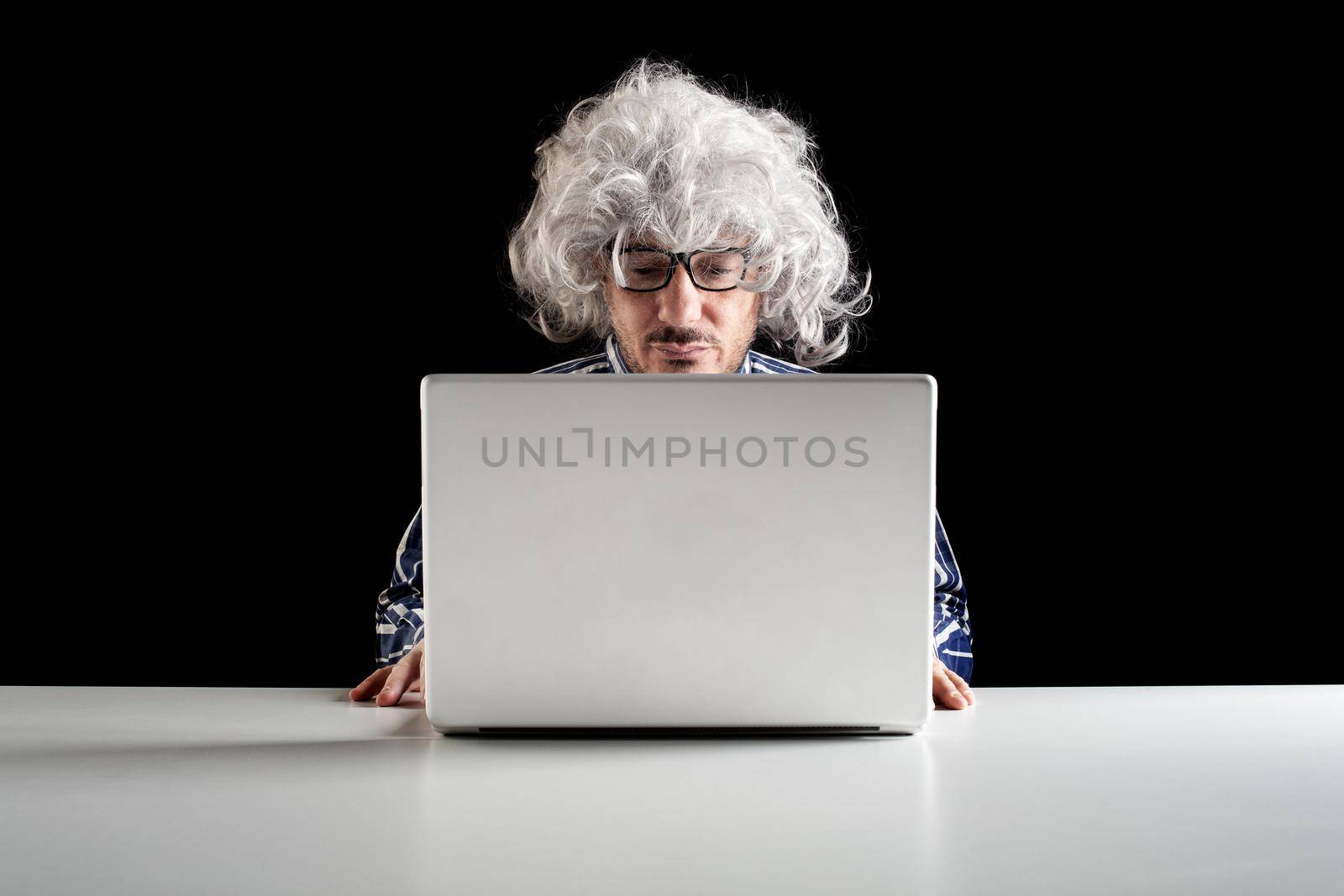 A boomer senior-focused concentrated sit at the desk looking at laptop computer on black background