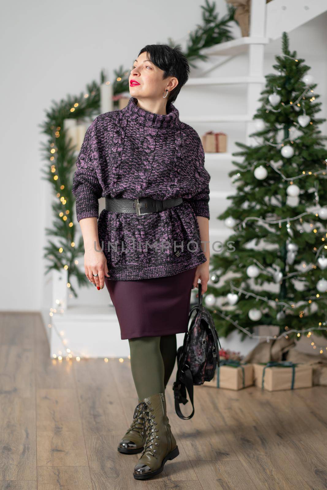 Smiling brunette woman with short hair, with tired eyes posing near the Christmas tree.