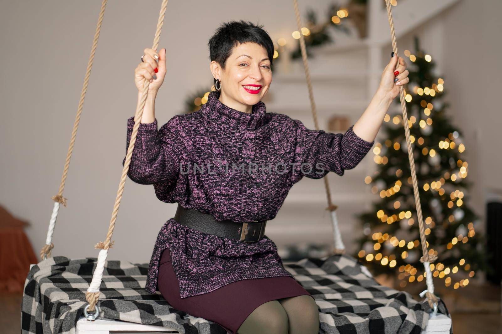 Smiling brunette woman with short hair, with tired eyes on a swing in the room.