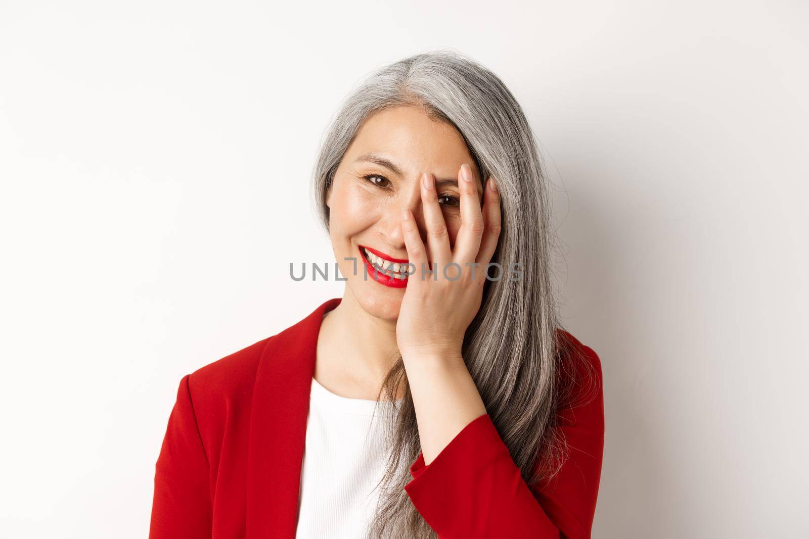 Beauty and makeup concept. Close up of beautiful asian mature woman, laughing and touching face, smiling happy, standing over white background.