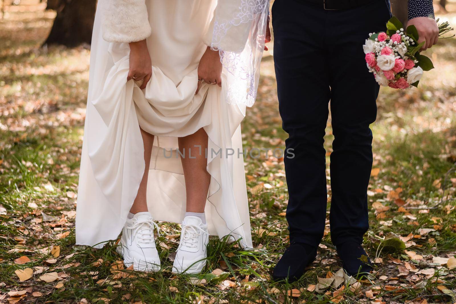the bride and groom with a bouquet of flowers in fall in the park. the bride lifted her skirt, showing white sneakers.