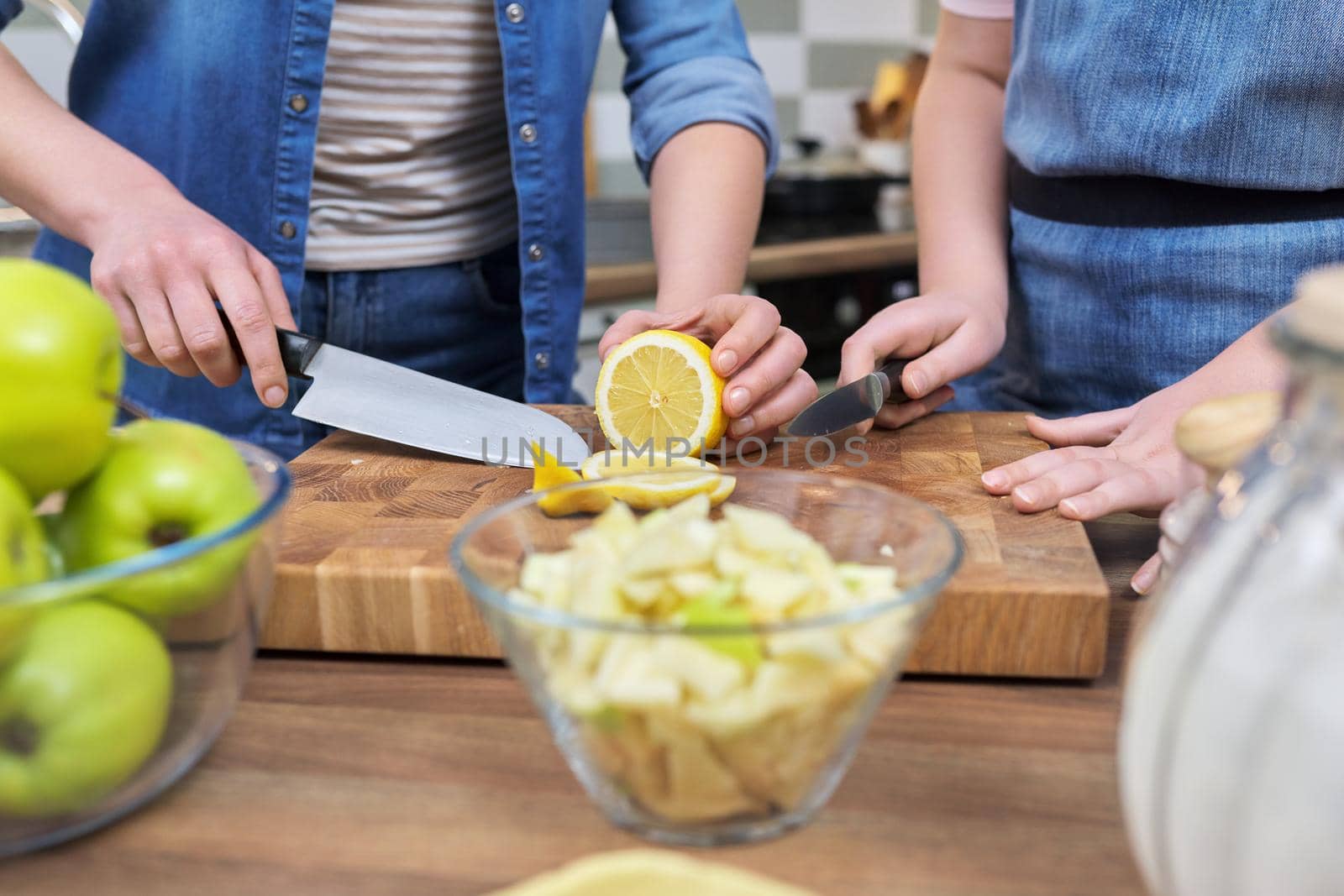Mom and teenage daughter preparing apple pie together, at home in the kitchen. Close up of hands cutting lemon