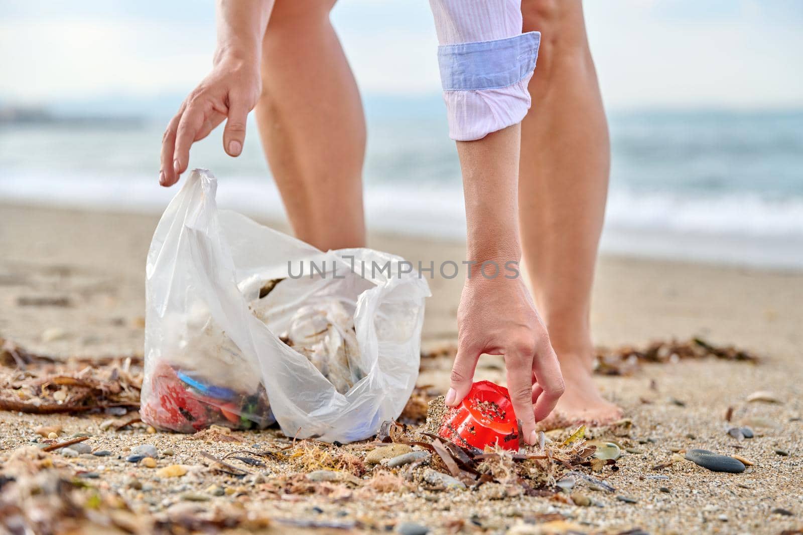 Close-up of a woman's hands picking up plastic trash into a bag on the beach. Environmental protection, pollution, people, nature, ecology concept