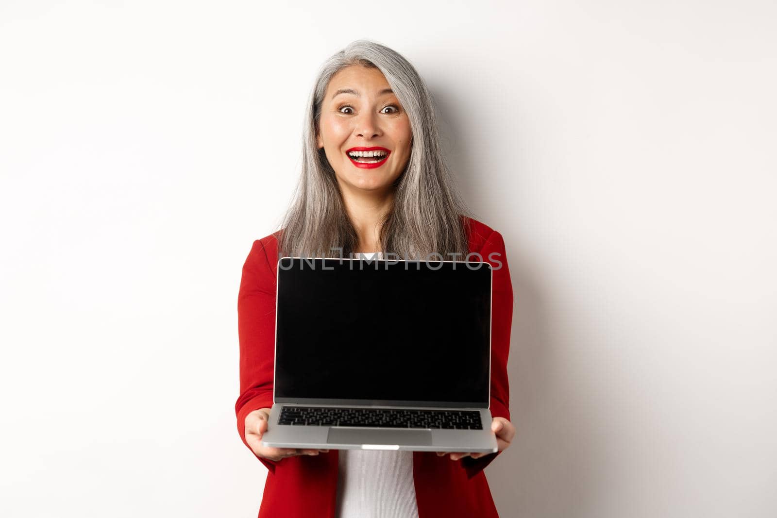 Business. Happy senior female entrepreneur demonstrate blank laptop screen, smiling amazed at camera, standing over white background.