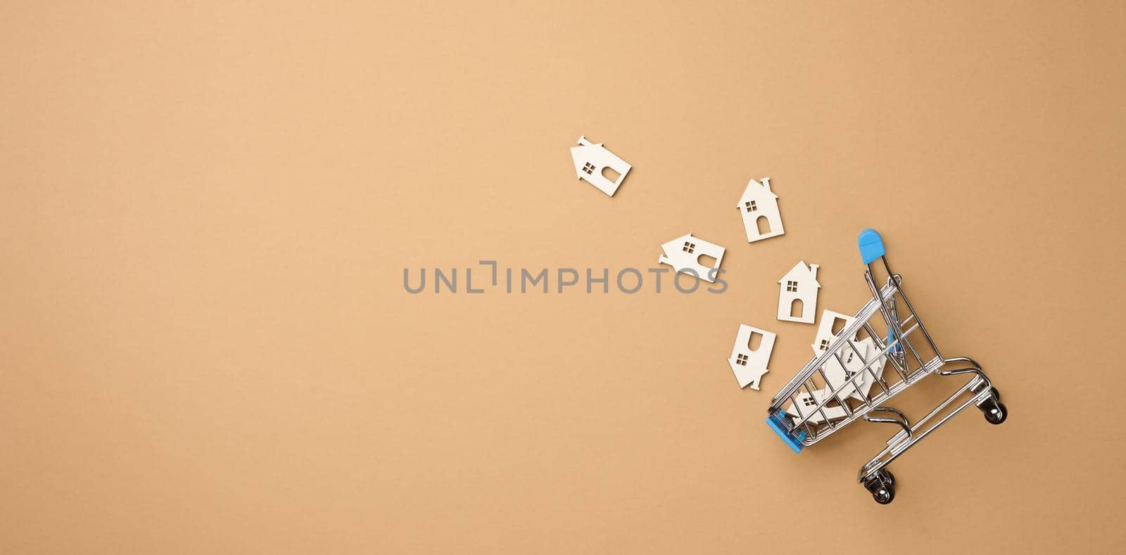 model of a wooden house and a metal miniature shopping cart on a light brown background, top view. Home search concept for rent, purchase, mortgage