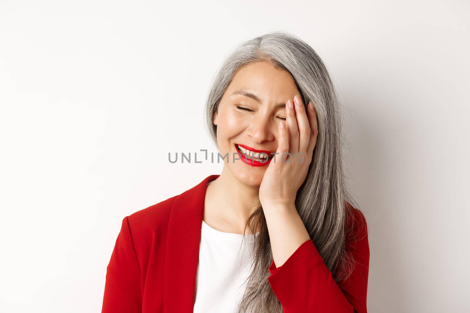 Beauty and makeup concept. Close up of beautiful asian mature woman, laughing and touching face, smiling happy, standing over white background.