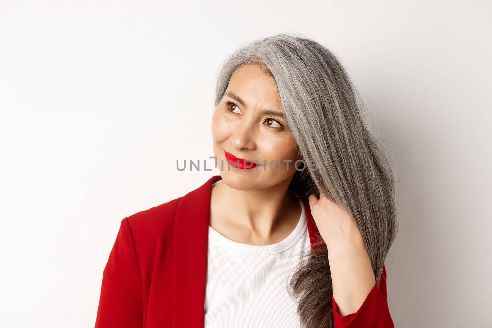 Beauty and haircare concept. Close up of elegant asian senior woman showing shiny and healthy grey hair, smiling and looking aside, white background by Benzoix