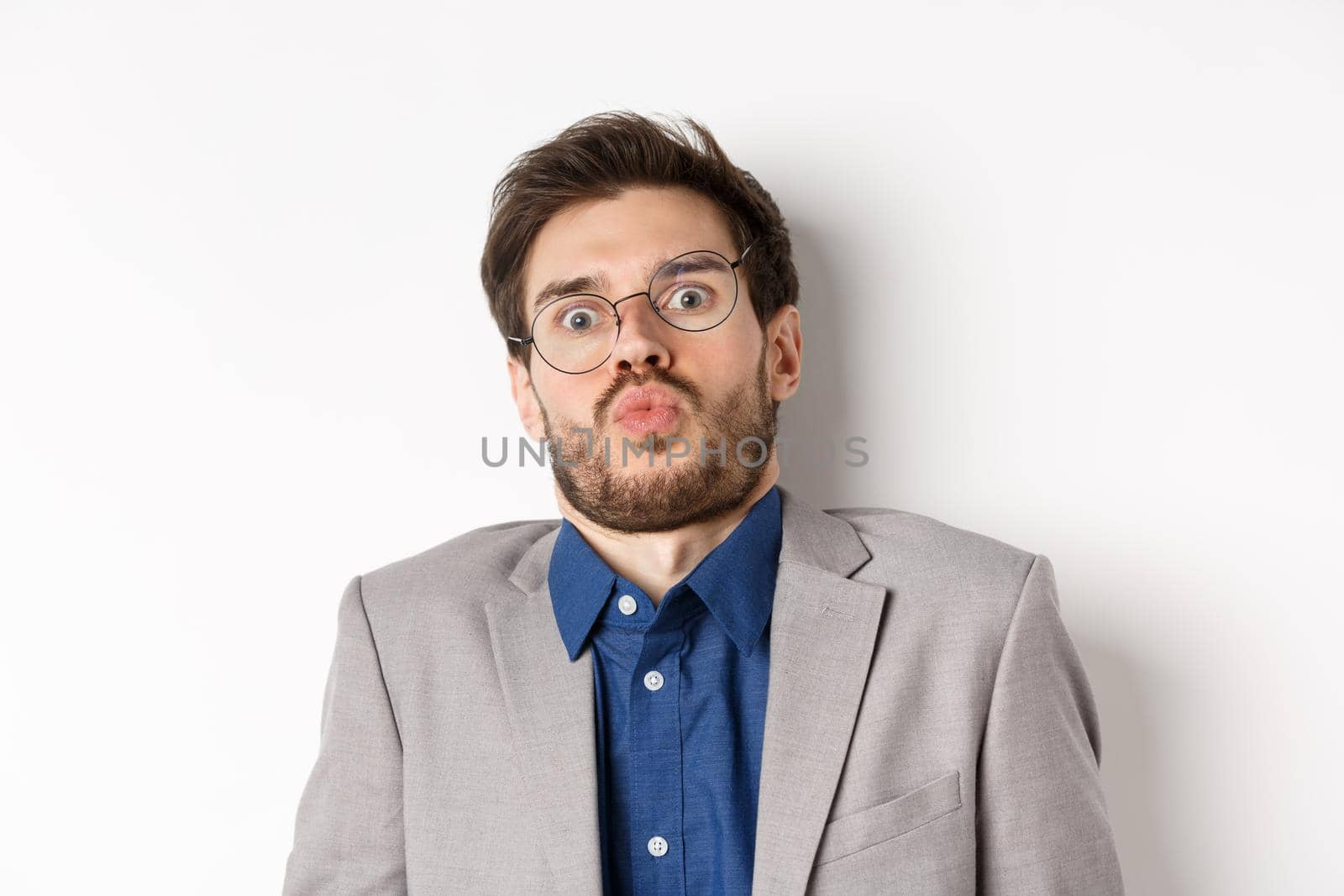 Startled guy in glasses and suit, tilt back and looking shocked or scared at camera, standing against white background.