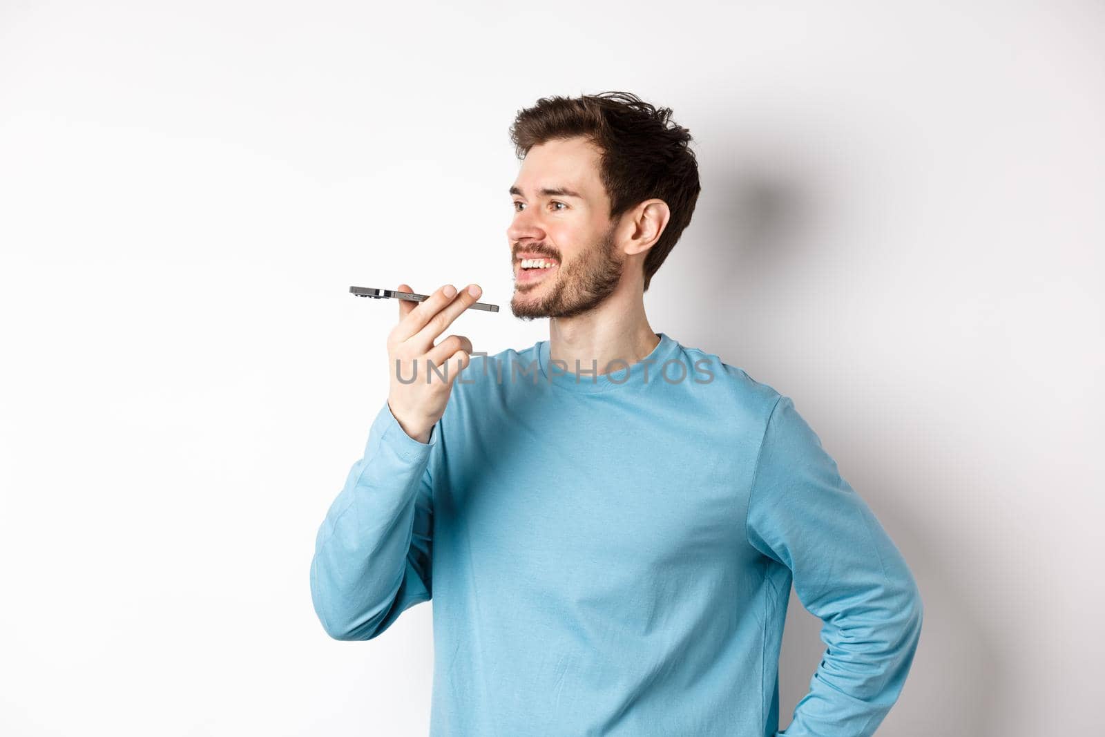 Young man talking on speakerphone or translating voice recording on application, standing happy on white background.
