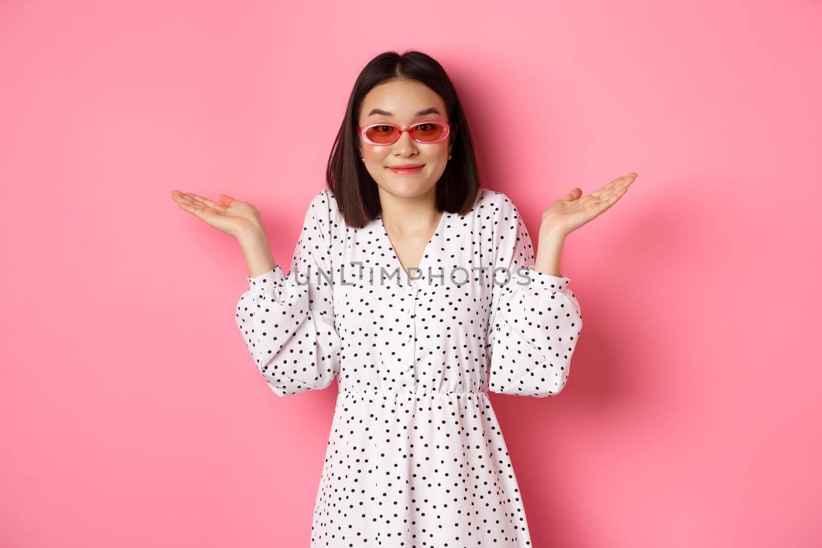 Cute asian woman tourist smiling at camera, shrugging clueless, dont know, wearing trendy sunglasses and white dress, standing against pink background by Benzoix
