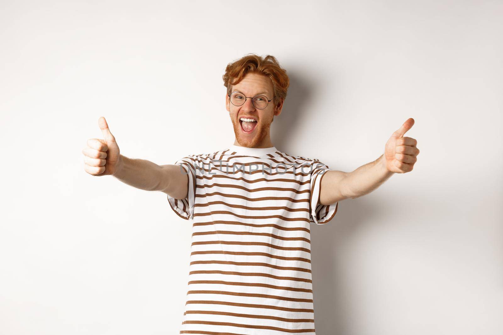 Happy redhead man scream yes and showing thumbs-up, approve and praise excellent company, standing over white background.