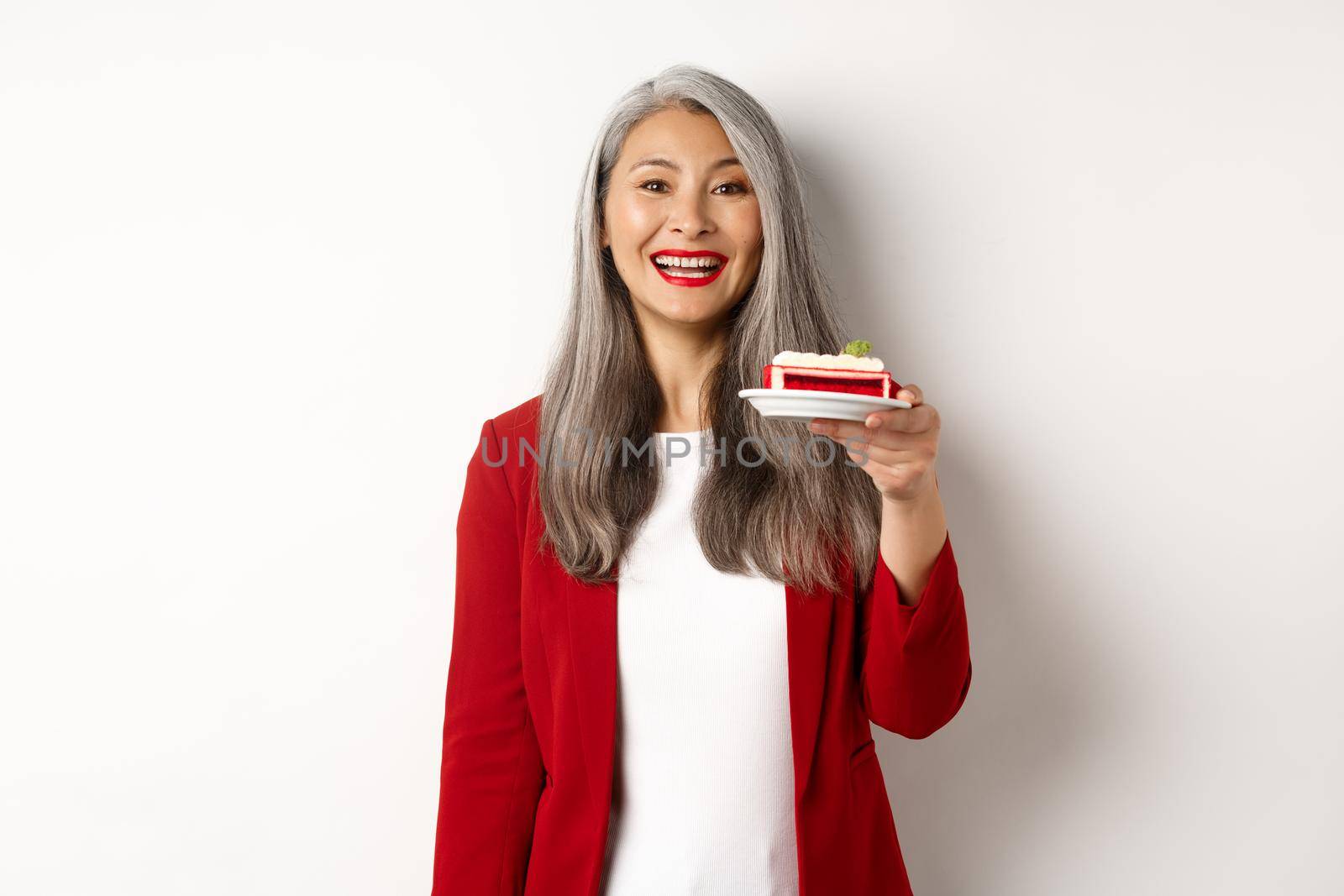 Celebration and holidays concept. Smiling asian businesswoman congratulate employees, giving plate with sweet cake and looking happy, standing over white background.