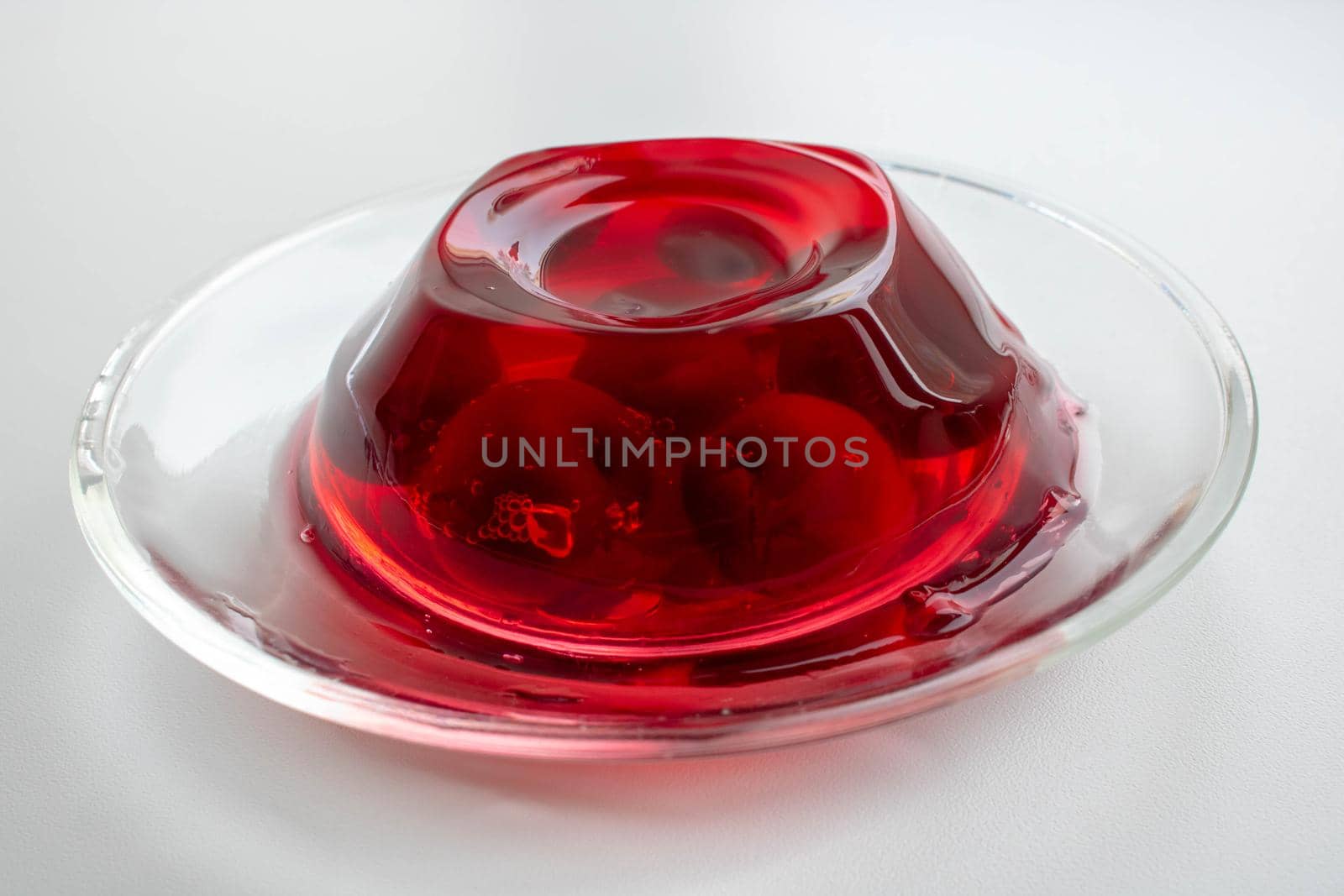 Glass plate with cherry berries in red jelly on a white background. by lapushka62