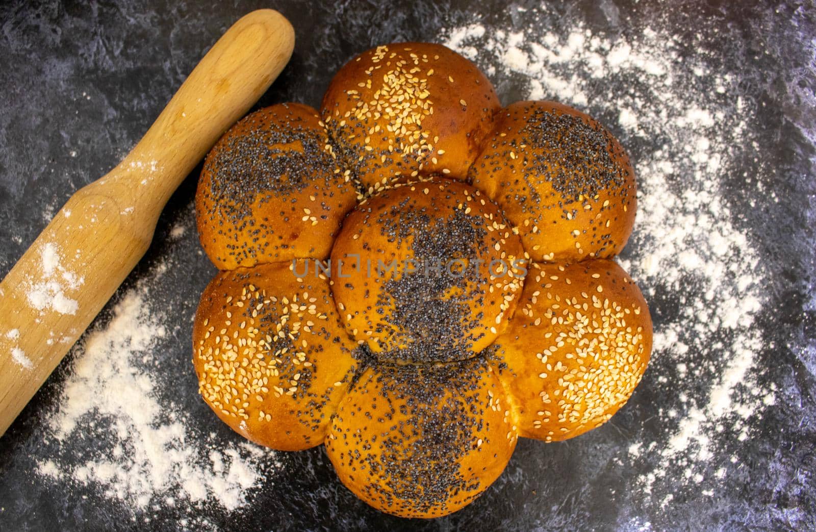 A freshly baked bread with poppy seeds and sesame seeds is on the dark table.