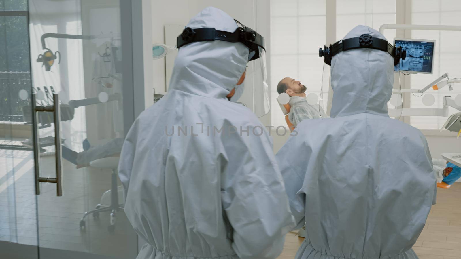 Orthodontist with ppe suit preparing for patient consultation using dental equipment and tools in oral cabinet. Dentist talking to assistant before starting teethcare examination