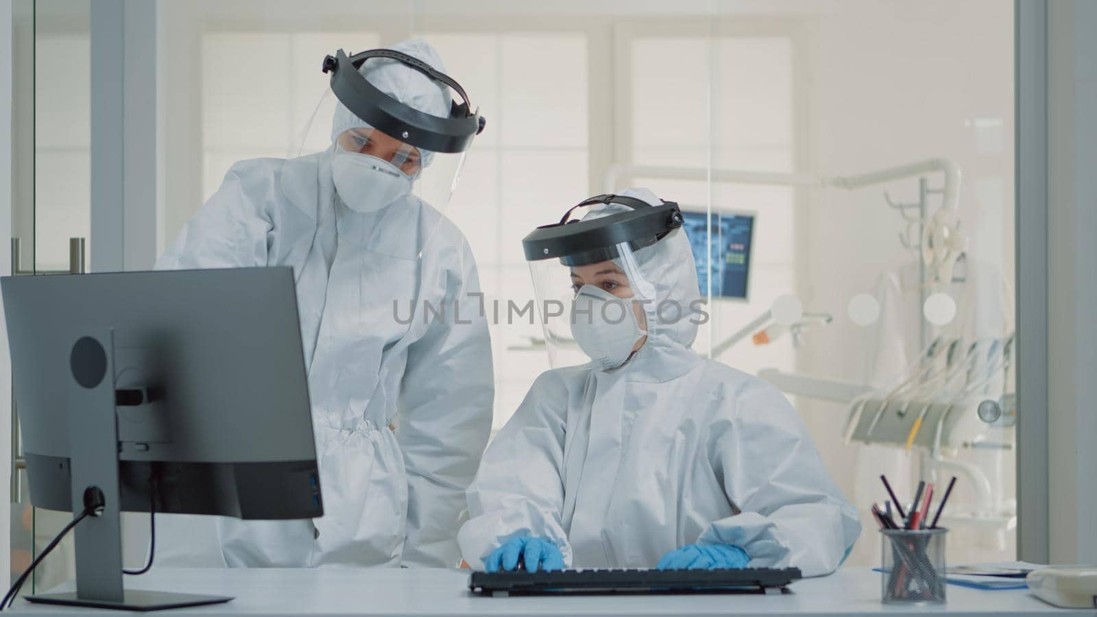 Dentistry team of specialists with ppe suits using computer for modern dental healthcare. Nurse sitting at desk, looking at monitor while dentist analyzing screen during covid pandemic