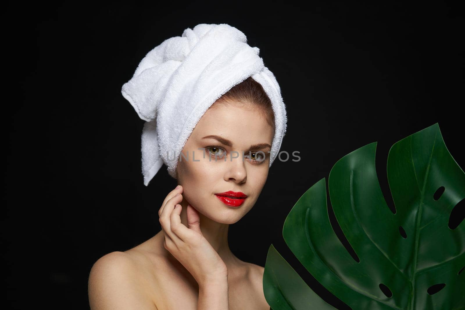attractive woman palm leaf bare shoulders clear skin dark background. High quality photo