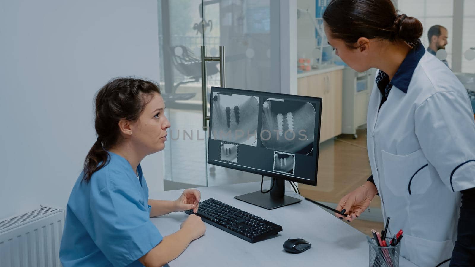 Stomatologist and nurse examining dental x ray scan on computer monitor for patient teethcare. Dentist and assistant at oral care clinic using device for radiography of dentition