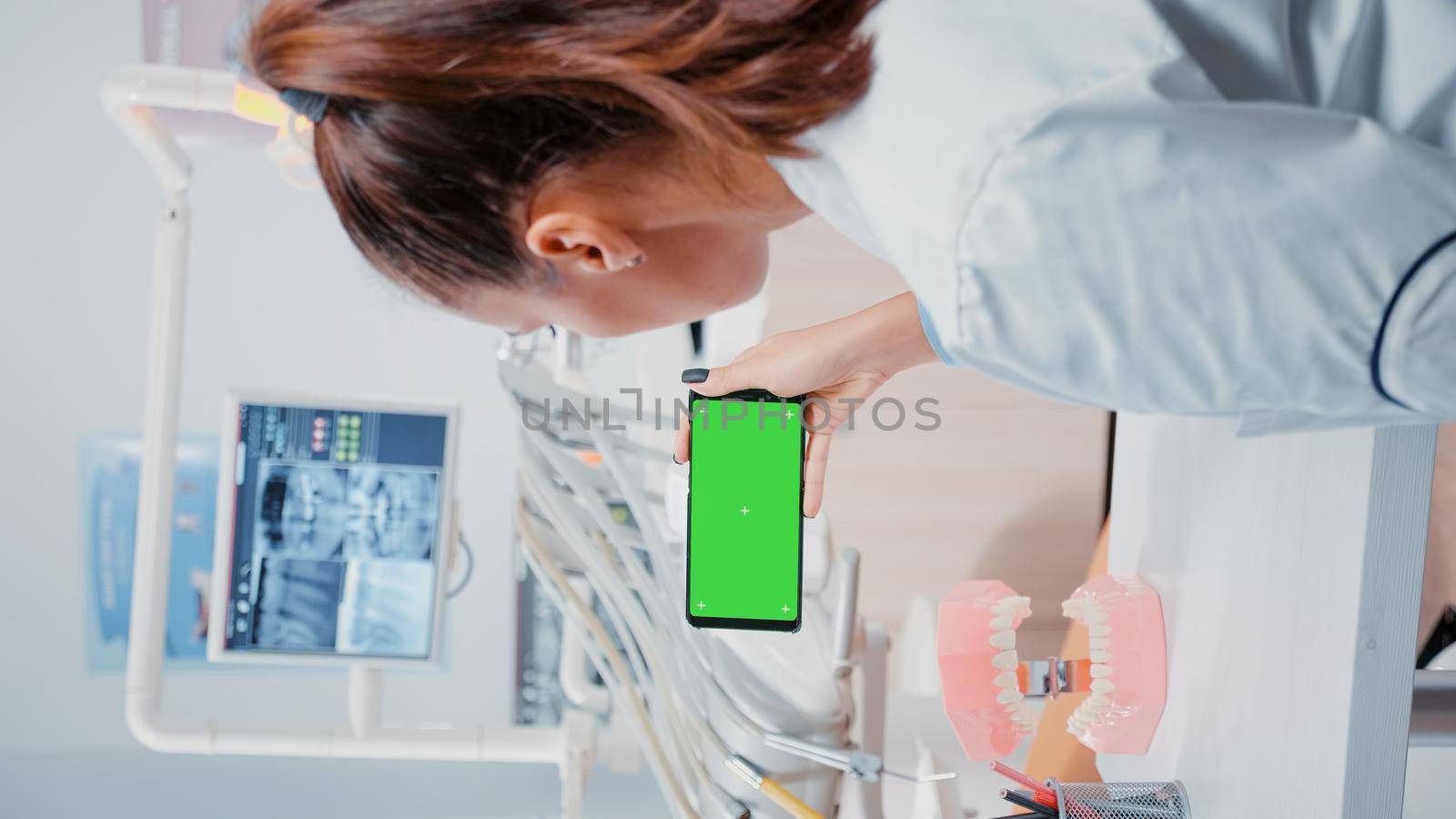 Vertical video: Specialist analyzing mobile phone with green screen for dental care. Dentist holding smartphone with chroma key on display for isolated background at stomatology clinic