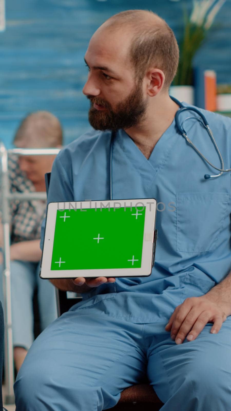 Man nurse and old patient looking at green screen on tablet in nursing home. Specialist holding horizontal chroma key with mockup template and isolated background. Medical assistant with device