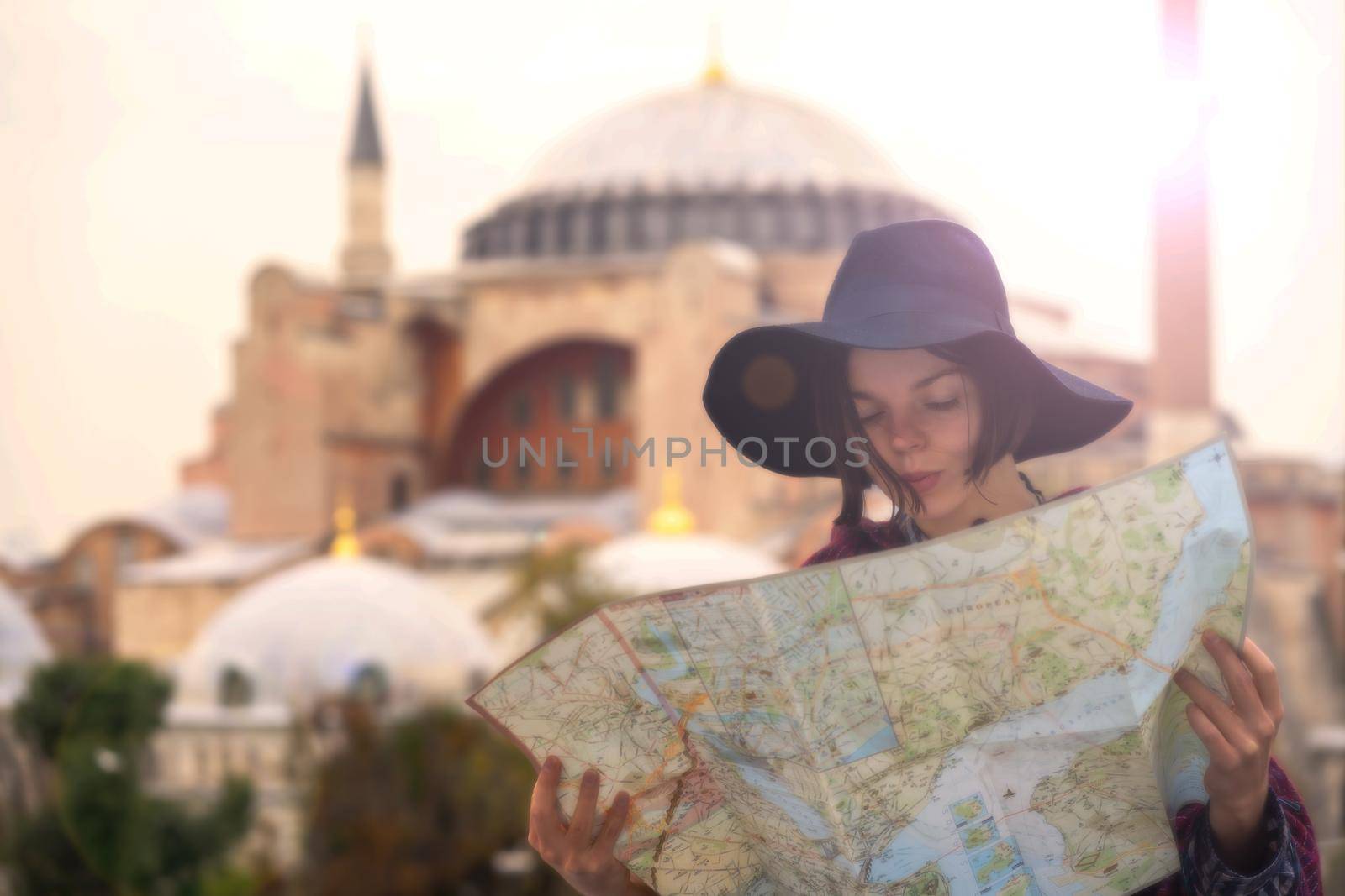 A young girl in a hat looks at a map of Istanbul on a sunny day. Beautiful ancient Hagia Sophia Mosque on the background. Traveling to Arab countries.