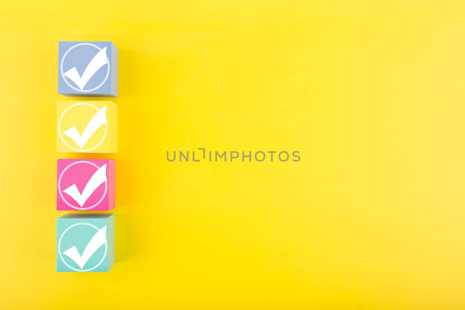 Four white checkmarks on multicolored toy cubes on bright yellow background with copy space. Concept of questionary, kids related checklist, to do list, planning, business or verification. 