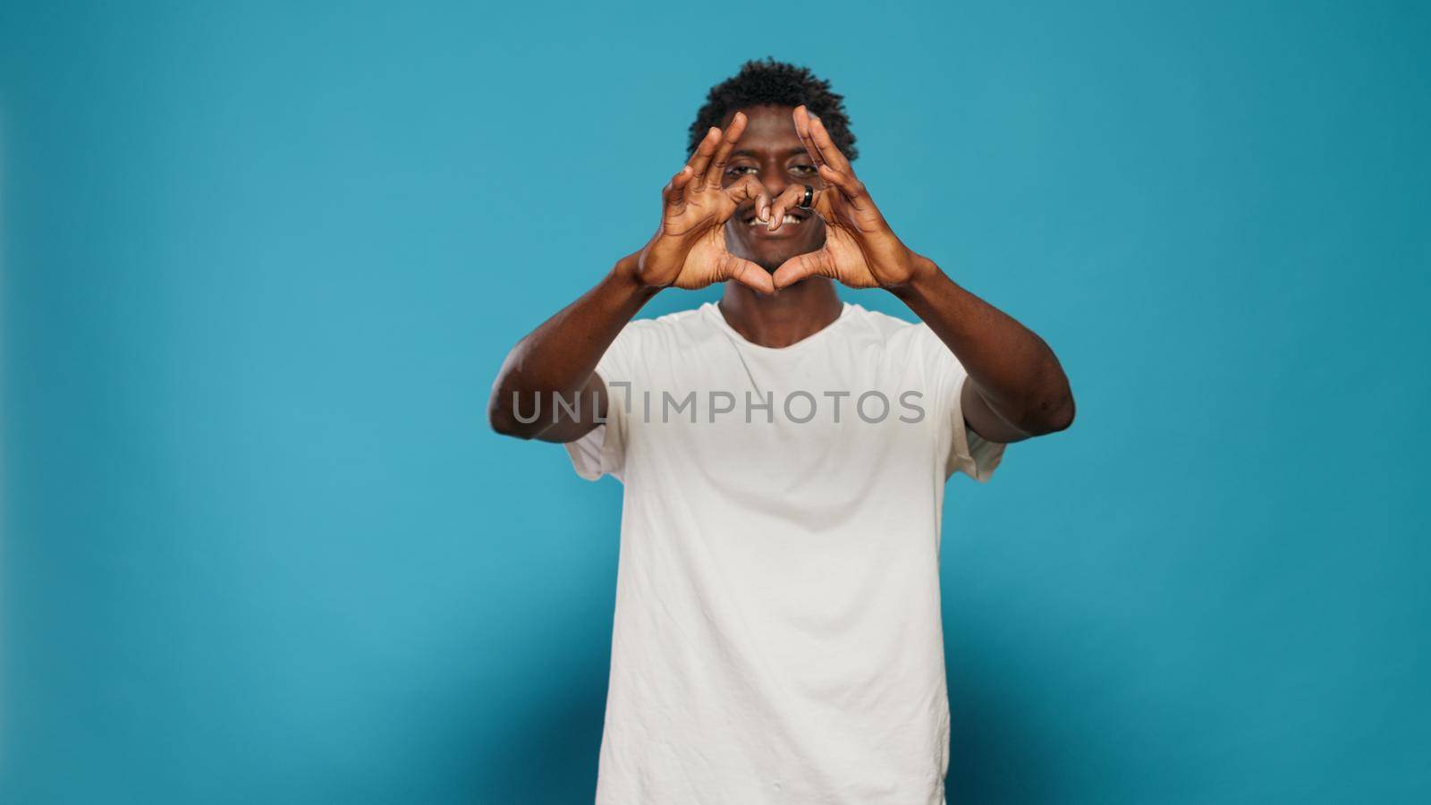 Joyful man doing heart shape symbol with hands while looking at camera. Romantic person showing love sign for valentines day. Adult celebrating romance with affectionate gesture.