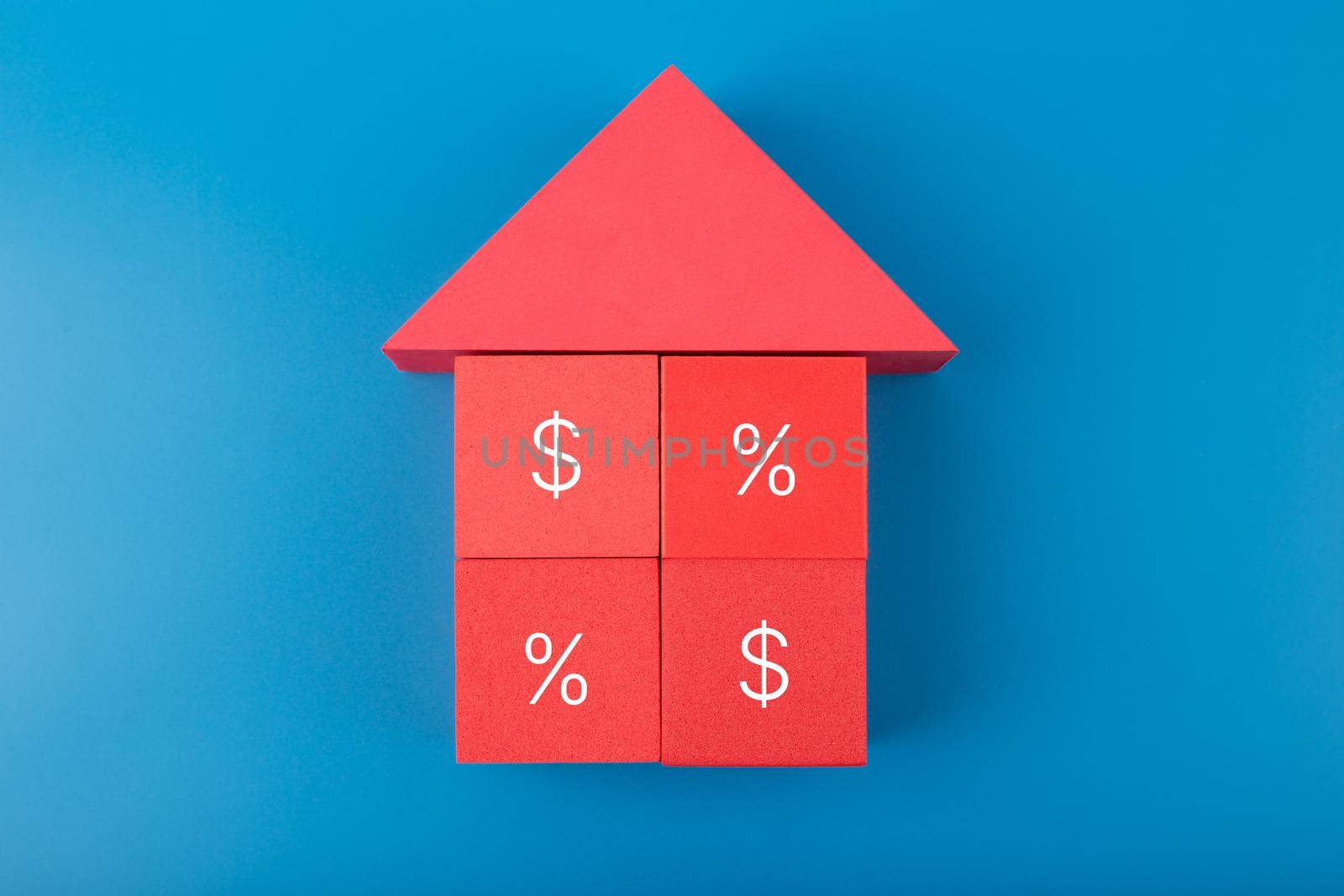 Red house made of toy cubes with percentage sign and dollar on blue background. Modern concept of inflation, percent, mortgage, interest rate growth and increasing