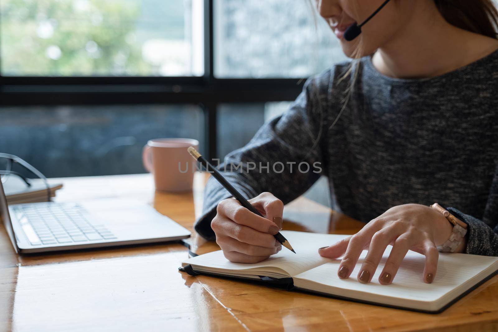 Close up hand of asian woman studying online from home making notes for student distance learning on laptop doing homework, watching listening video lesson. Remote education concept by nateemee