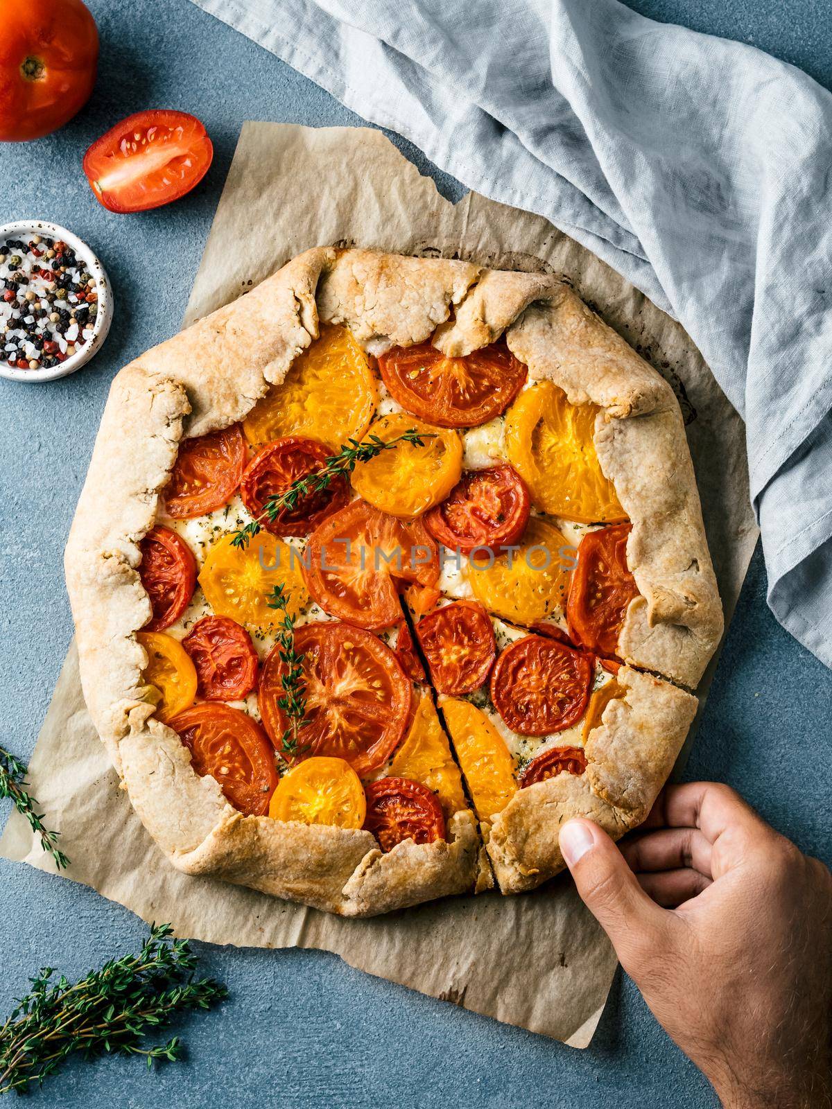 Savory fresh homemade tomato tart or galette.Hand takes piece of pie.Ideas and recipes healthy lunch,appetiezer-whole wheat or rye-wheat pie with tomatoes and cheese.Harvest tomatoes.Top view.Vertical