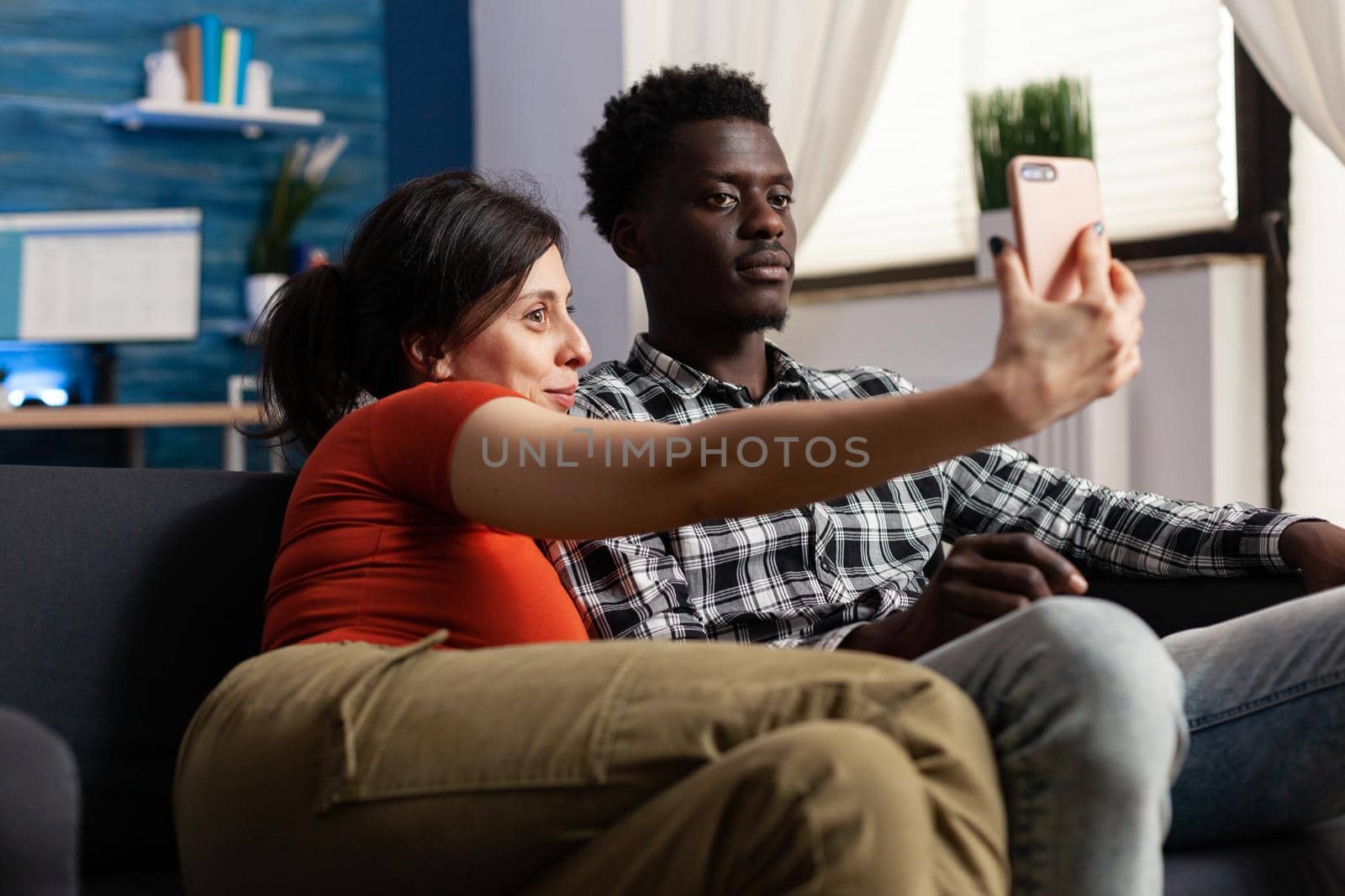 Joyful interracial couple taking selfies together at home by DCStudio