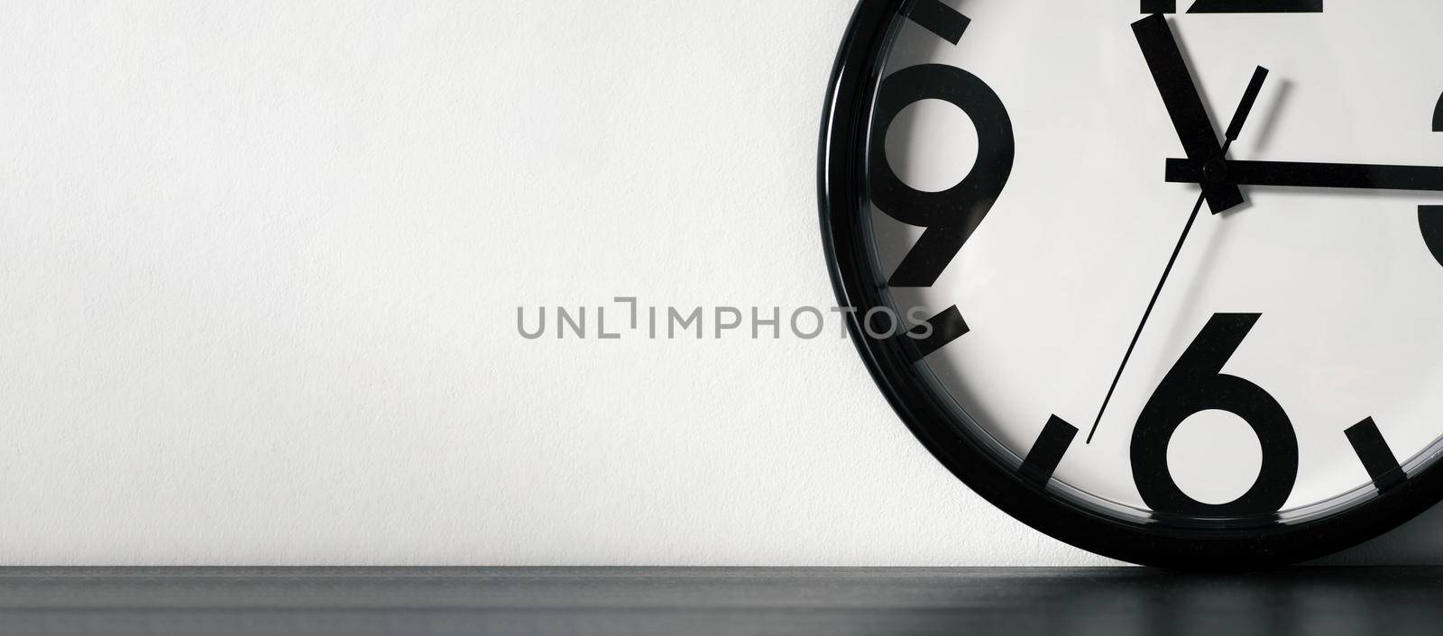 Modern minimalistic clock or simple white and black on black wooden table and white wall with space for text. Long horizontal banner