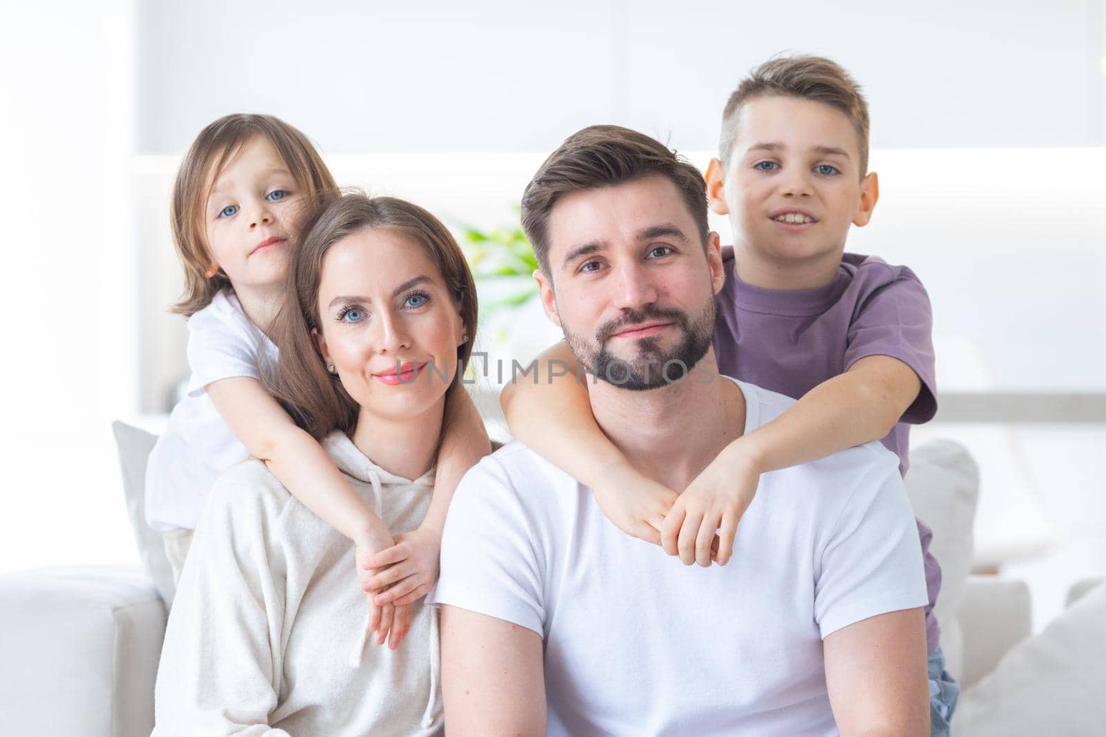 Family portrait of young parents with their two children at home, white modern desgin of living room