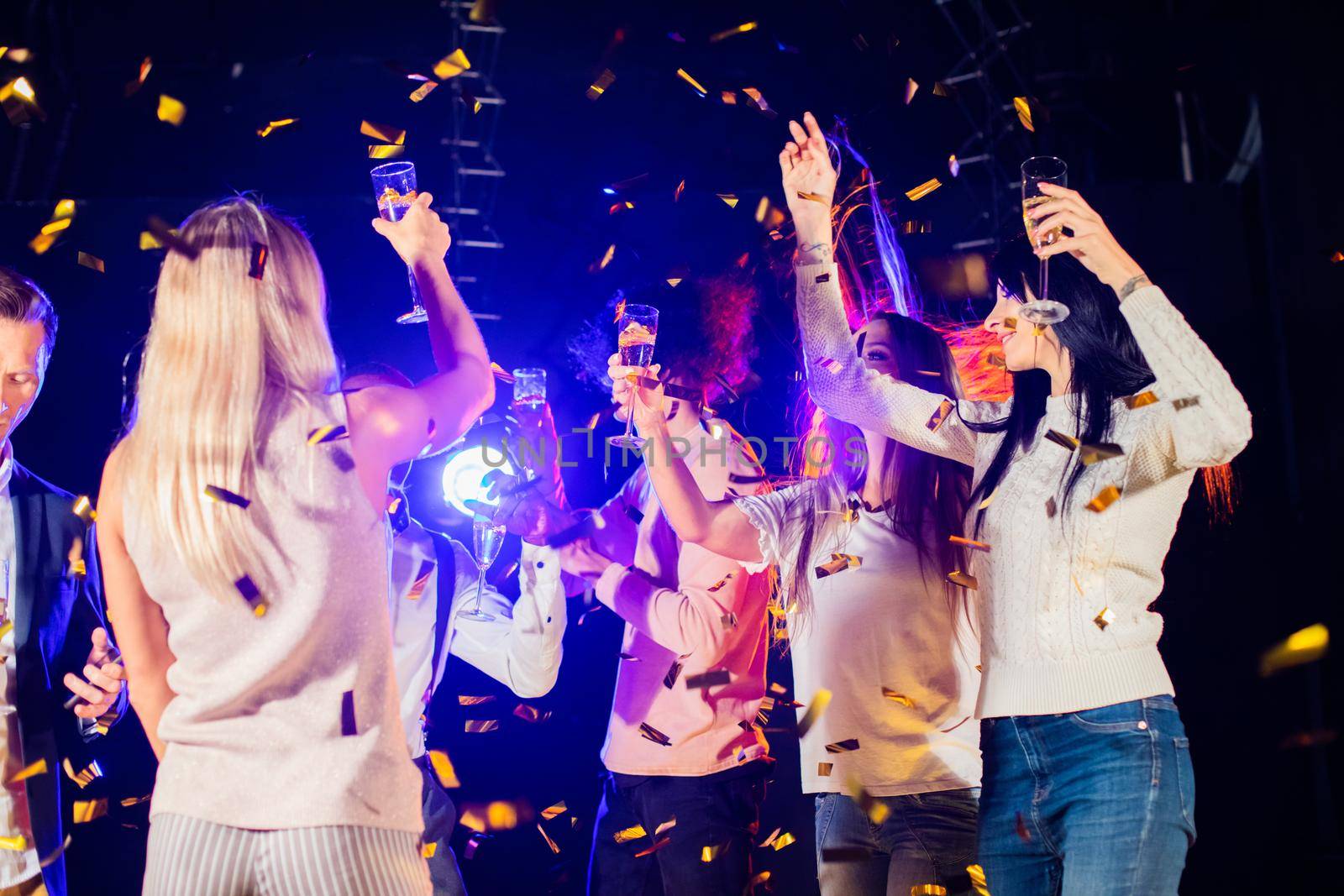 People dance at party in nightclub, drink champagne in falling confetti