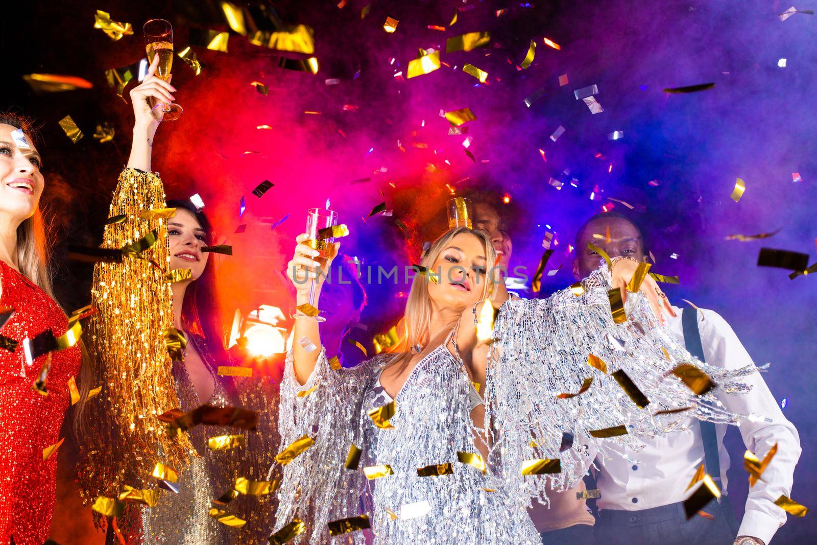 People dance at party in nightclub, drink champagne in falling confetti