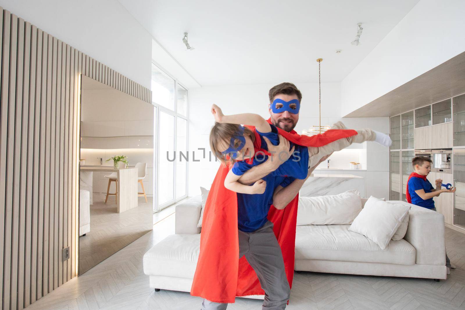 Father holding son flying in superhero costume at home