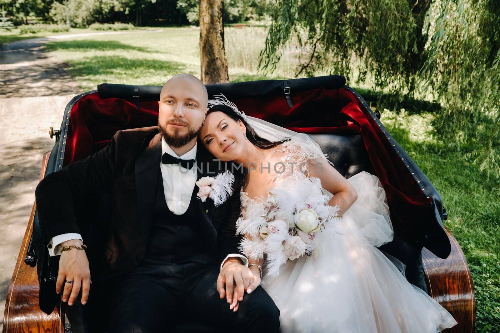 The bride and groom with a bouquet are sitting in a carriage in nature in retro style by Lobachad